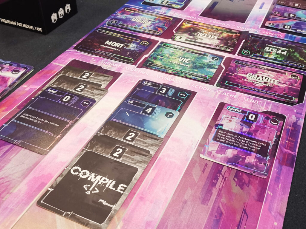 Une partie de Compile en cours, avec les protocoles et les cartes commandes étalées sur le tapis de jeu